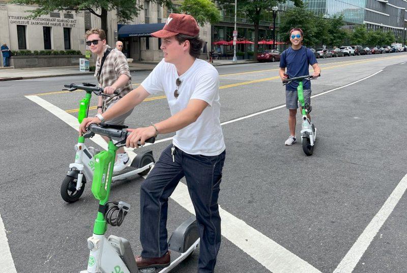 学生 riding e-scooters pause on a city street. 